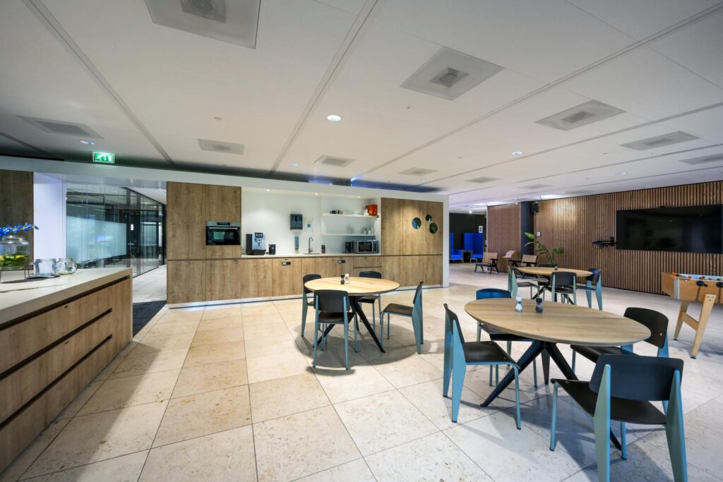 Modern office break area on Gustav Mahlerlaan with round tables, kitchen amenities, and a foosball table.